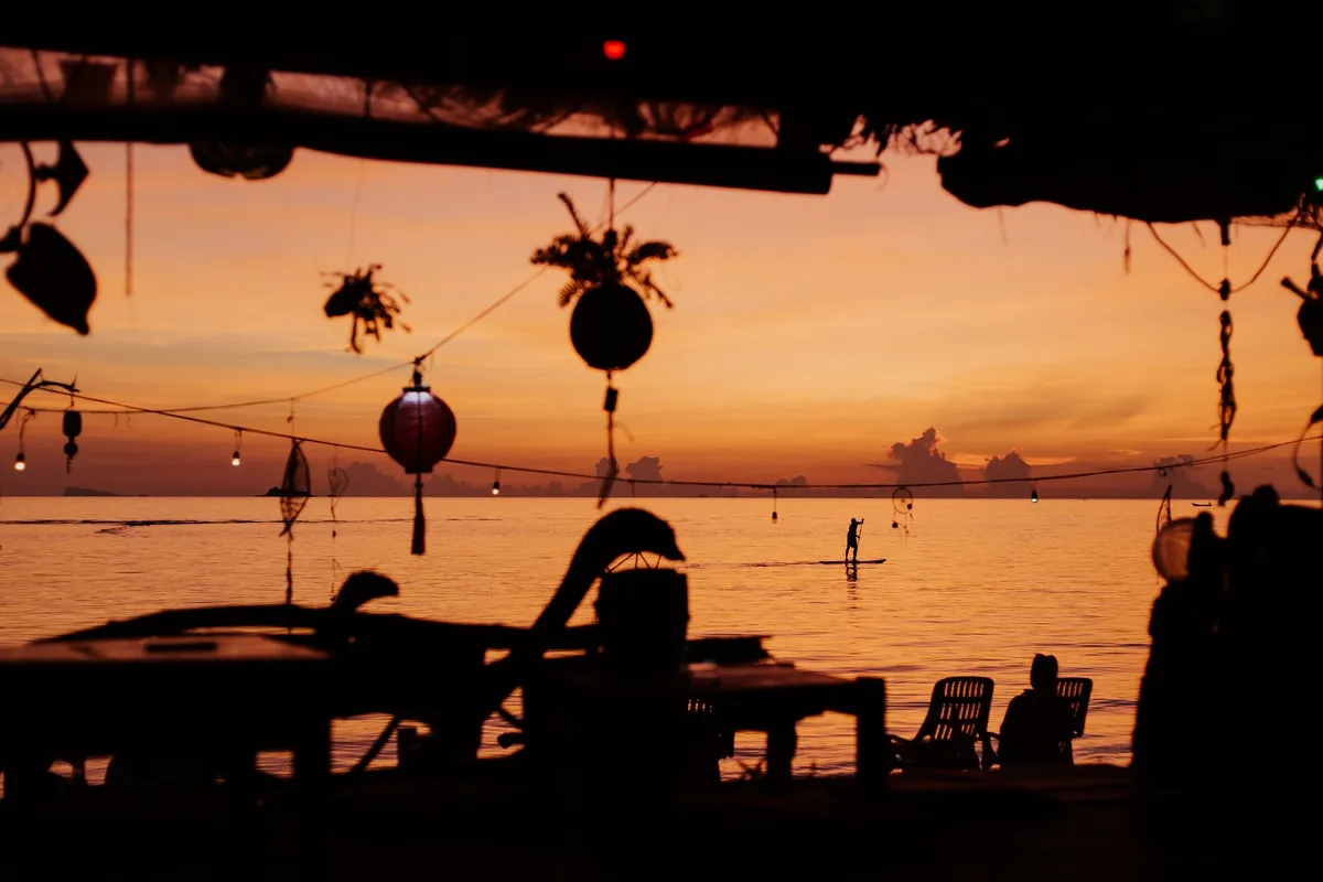 Bar de praia com mesas voltadas para o mar ao pôr do sol
