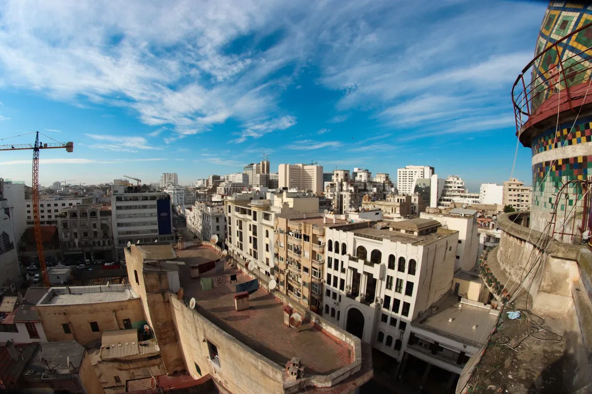 Skyline urbano de Casablanca com prédios modernos e a Mesquita Hassan II ao fundo.