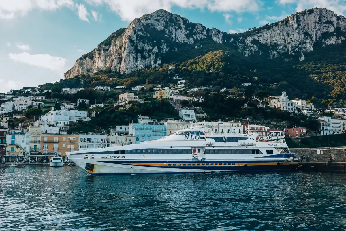 Barco de excursão ancorado no porto da ilha de Capri, com penhascos ao fundo
