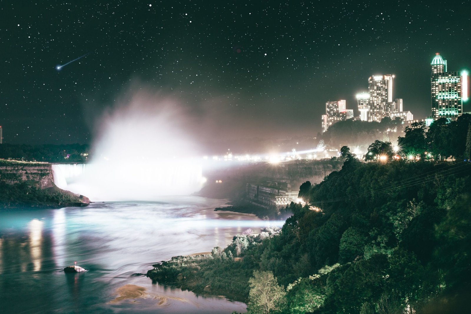 Cataratas do Niágara iluminadas à noite com o horizonte da cidade ao fundo