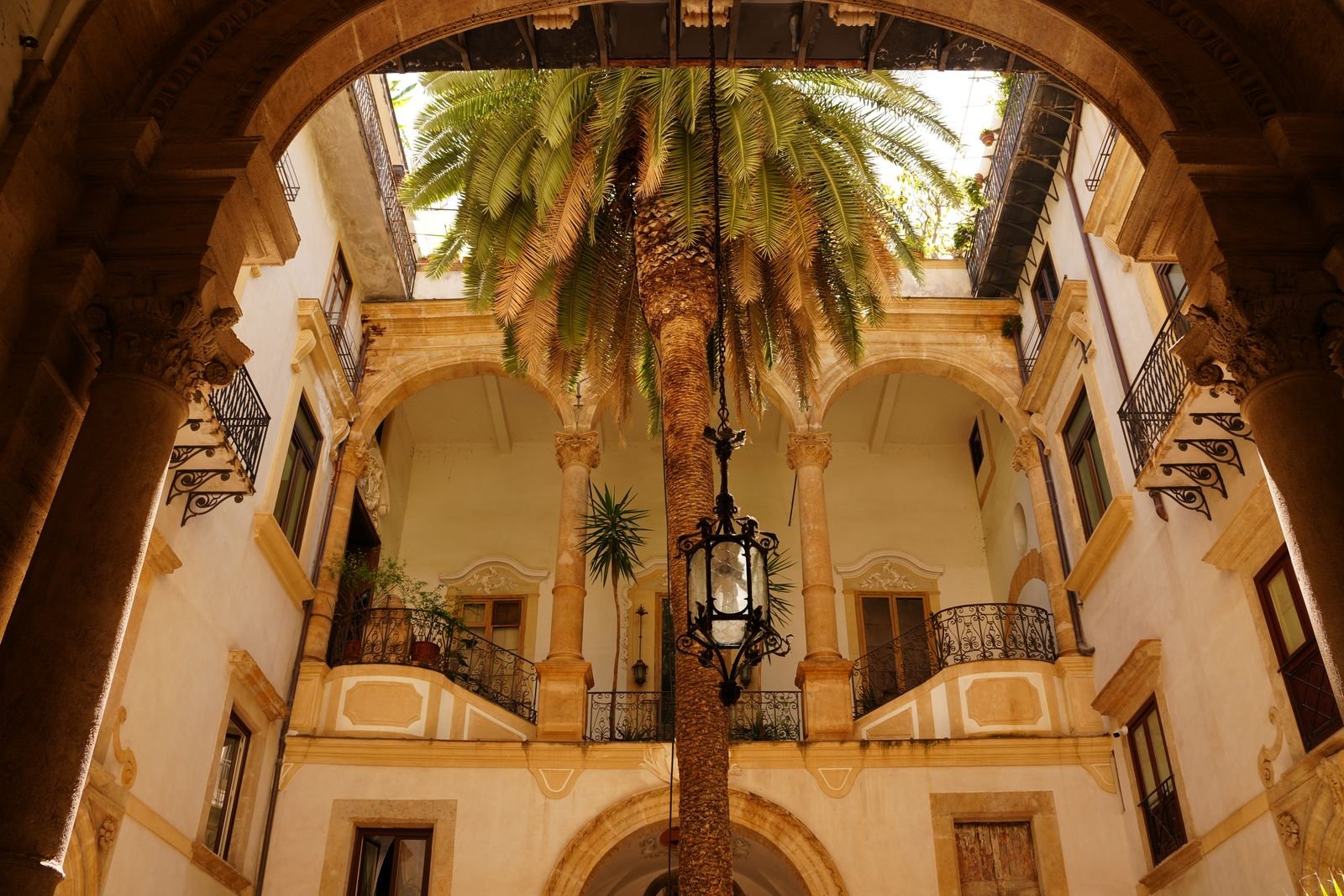 Pátio histórico de Palermo com arcadas, palmeira e varandas