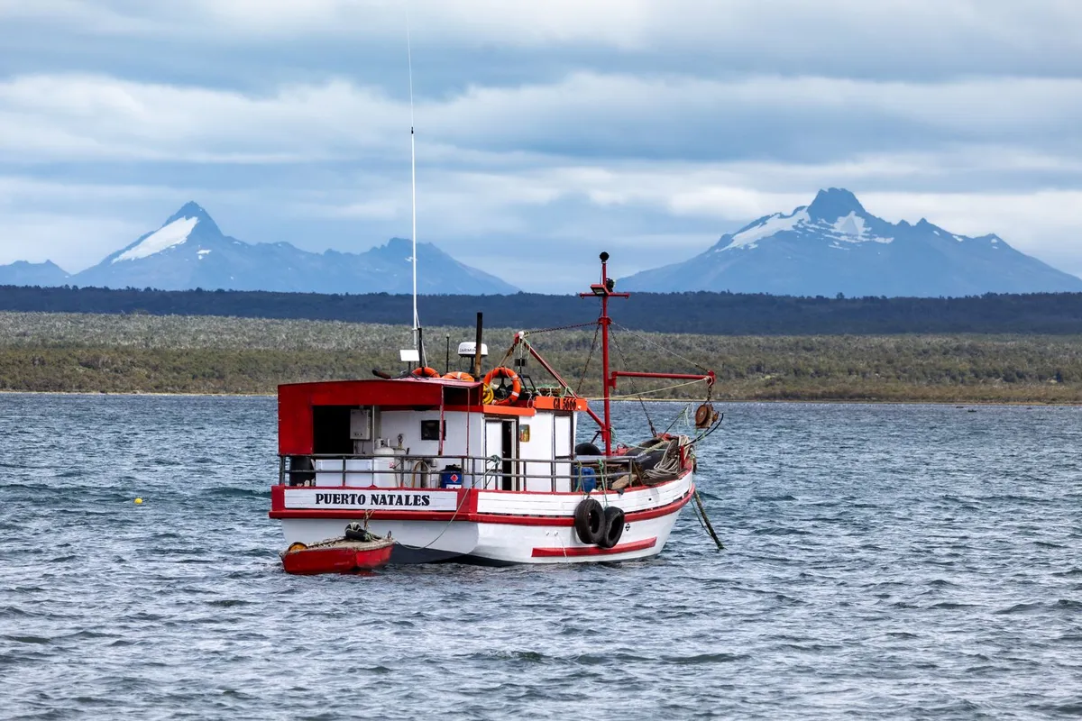 Barco no fiorde de Puerto Natales com montanhas ao fundo
