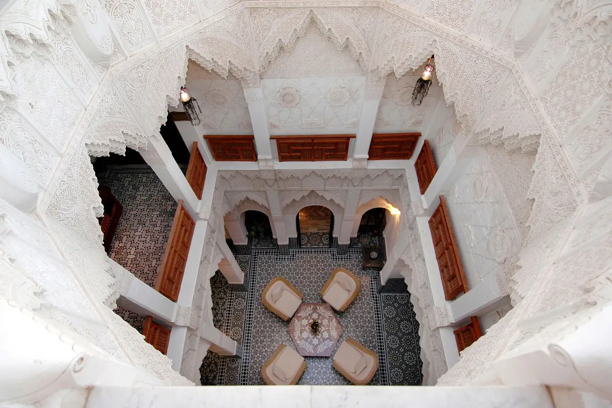 Pátio interno de um riad em Marrakech com fonte central, arcos entalhados e azulejos.