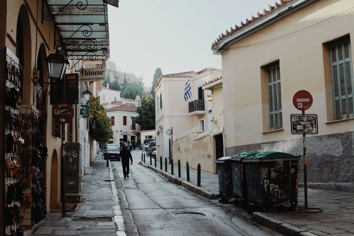 Rua estreita de pedra no bairro de Plaka, em Atenas, com casas neoclÃ¡ssicas