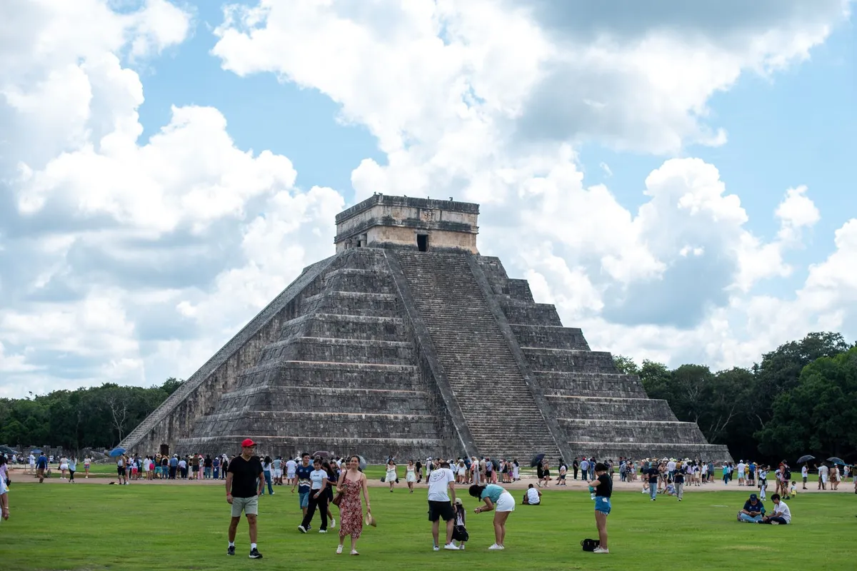 Turistas caminhando em frente à pirâmide El Castillo em Chichén Itzá