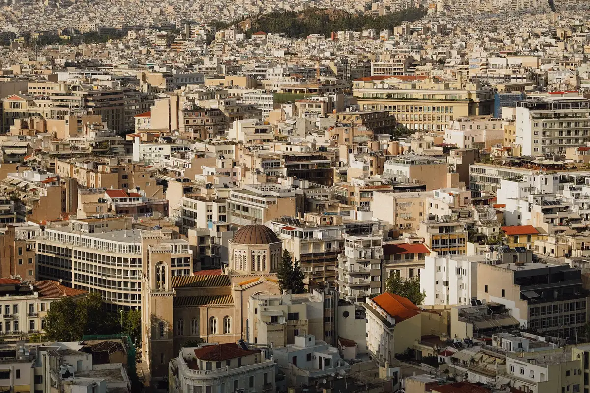Vista aÃ©rea do centro de Atenas com prÃ©dios brancos e o mar ao fundo