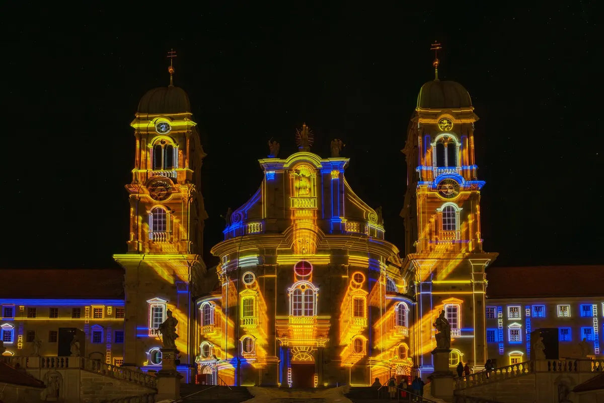 Fachada de igreja histórica iluminada por projeções coloridas à noite