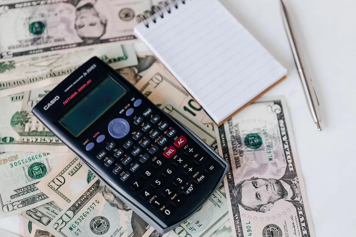 Calculadora e bloco de notas sobre notas de dólar para calcular o custo total da viagem