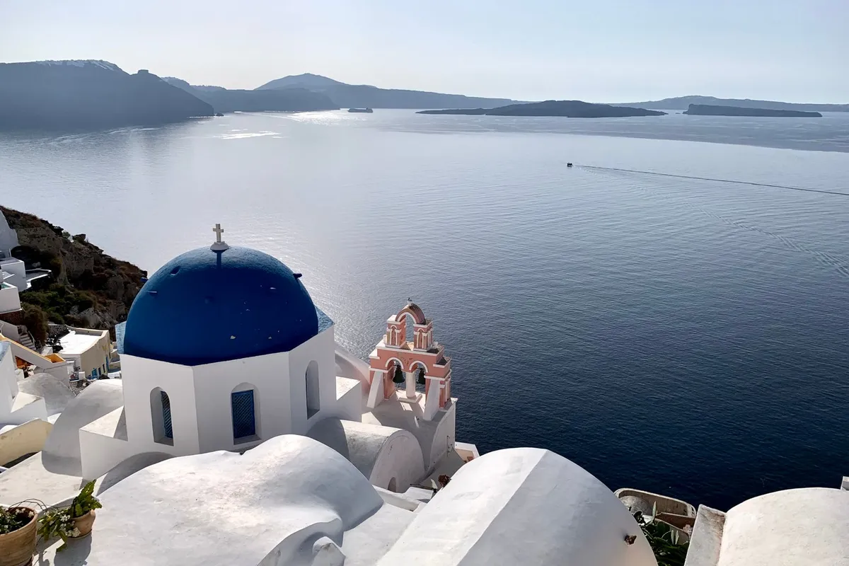 Igreja de cúpula azul em Santorini, na Grécia, com o mar Egeu ao fundo