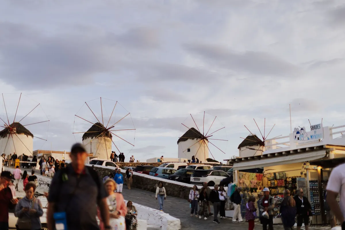 Turistas junto aos moinhos de vento de Mykonos ao pôr do sol