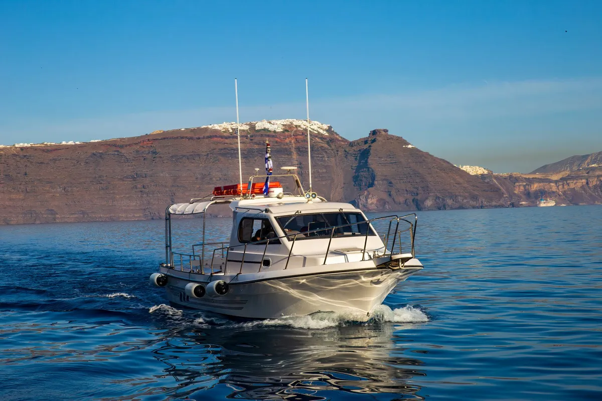 Barco branco navegando pela Caldeira de Santorini com falésias ao fundo