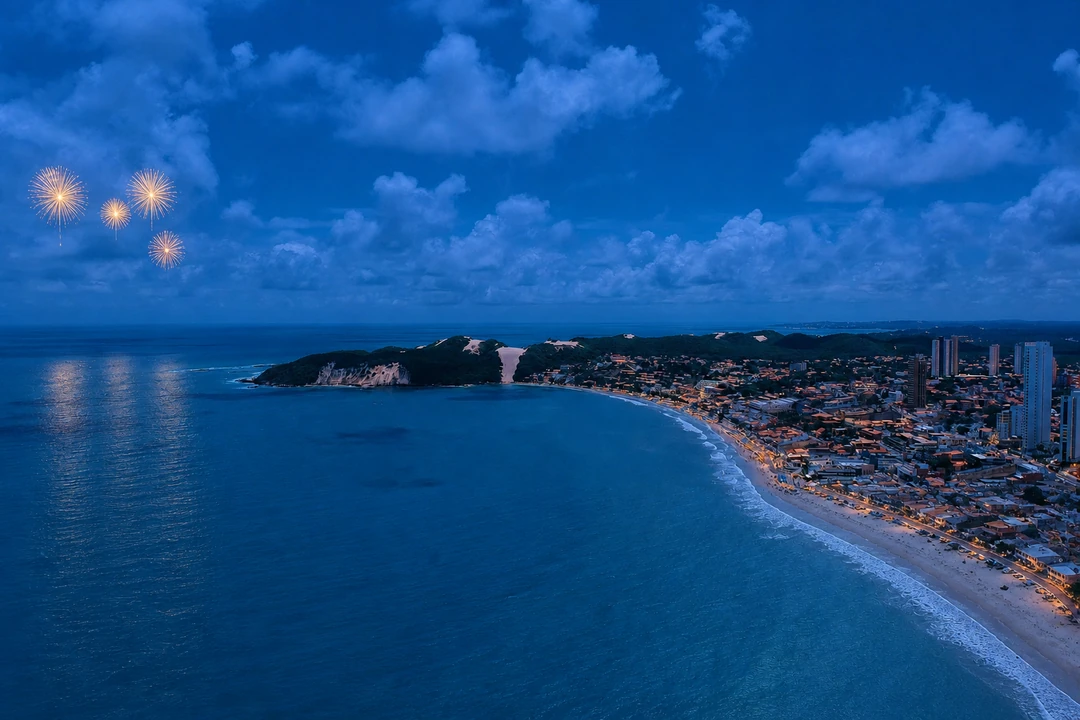 Vista aérea de Ponta Negra e do Morro do Careca ao anoitecer, com fogos ilustrativos sobre o mar
