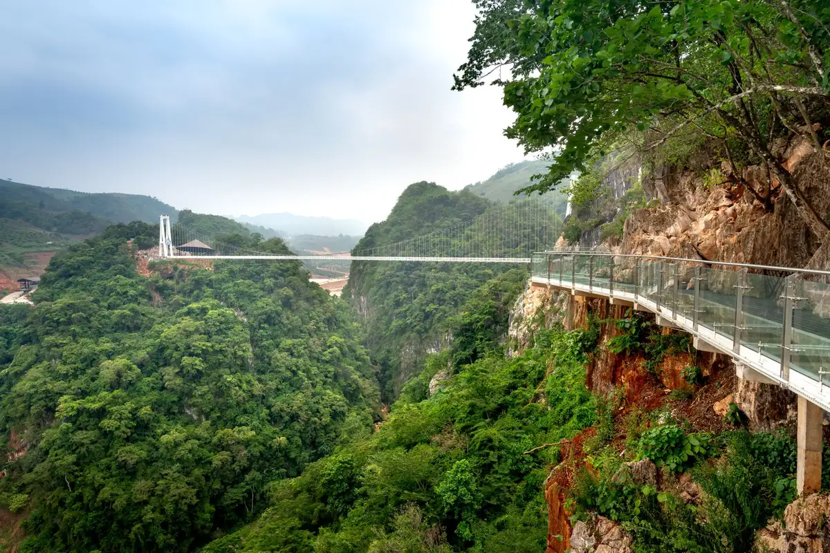Passarela de vidro suspensa sobre paisagem montanhosa, similar ao mirante de vidro dos Altos do Corvo Branco em Urubici