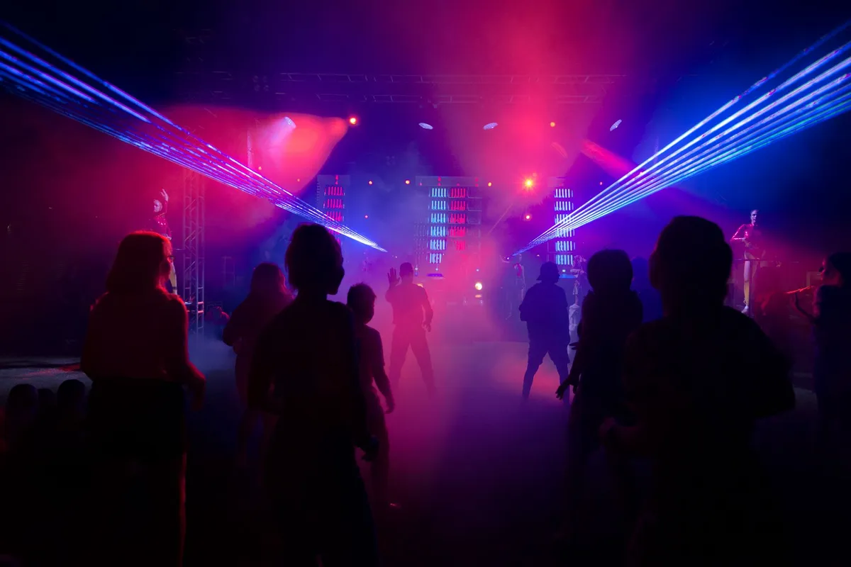 Multidão dança em festival de música eletrônica com luzes de palco