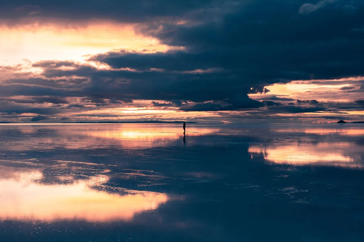Pessoa diante do reflexo no Salar de Uyuni ao entardecer
