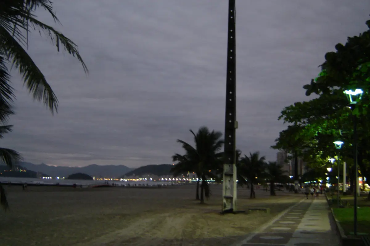 Orla da praia de Santos ao anoitecer, com palmeiras e prédios