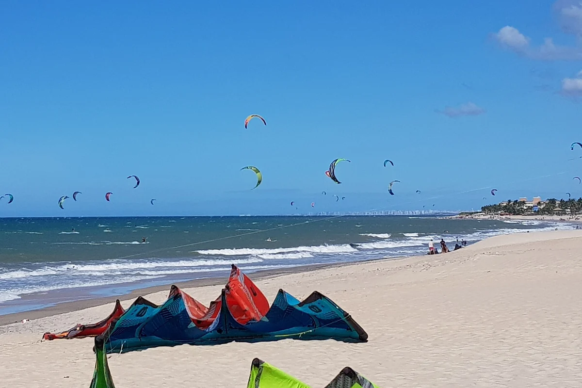 Praia de Cumbuco com pipas de kitesurf sobre o mar e equipamentos na areia