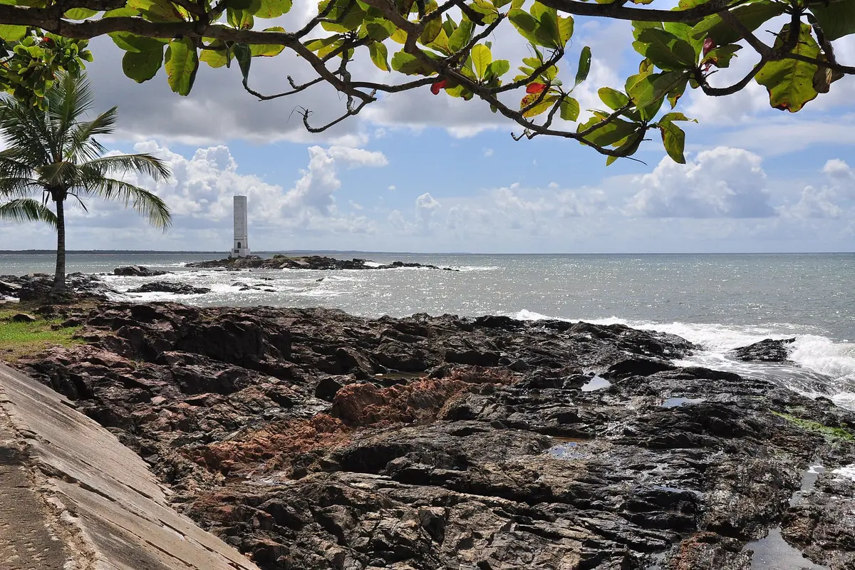 Farol branco da Praia da Concha em Itacaré, cercado por mar e pedras