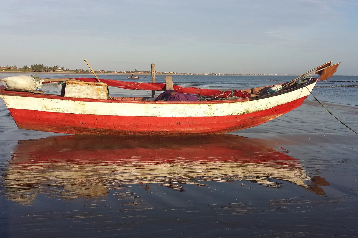 Barco vermelho e branco na faixa de areia molhada da Praia do Coqueiro
