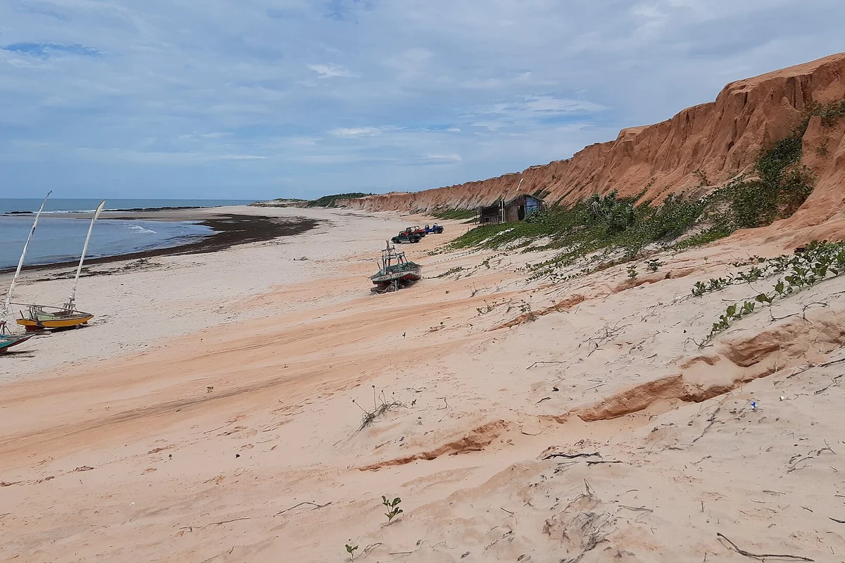 Falésias avermelhadas e praia de Canoa Quebrada com jangadas na areia