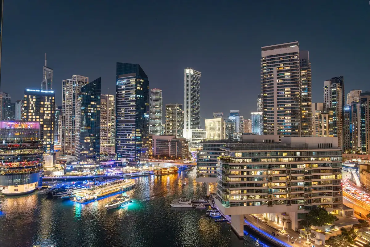 Dubai Marina iluminada à noite com arranha-céus, barcos e calçadão