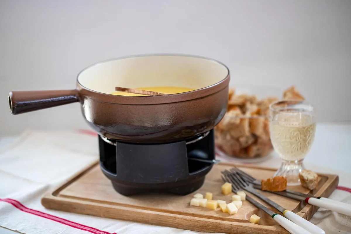 Panela de fondue de queijo com pães e utensílios à mesa