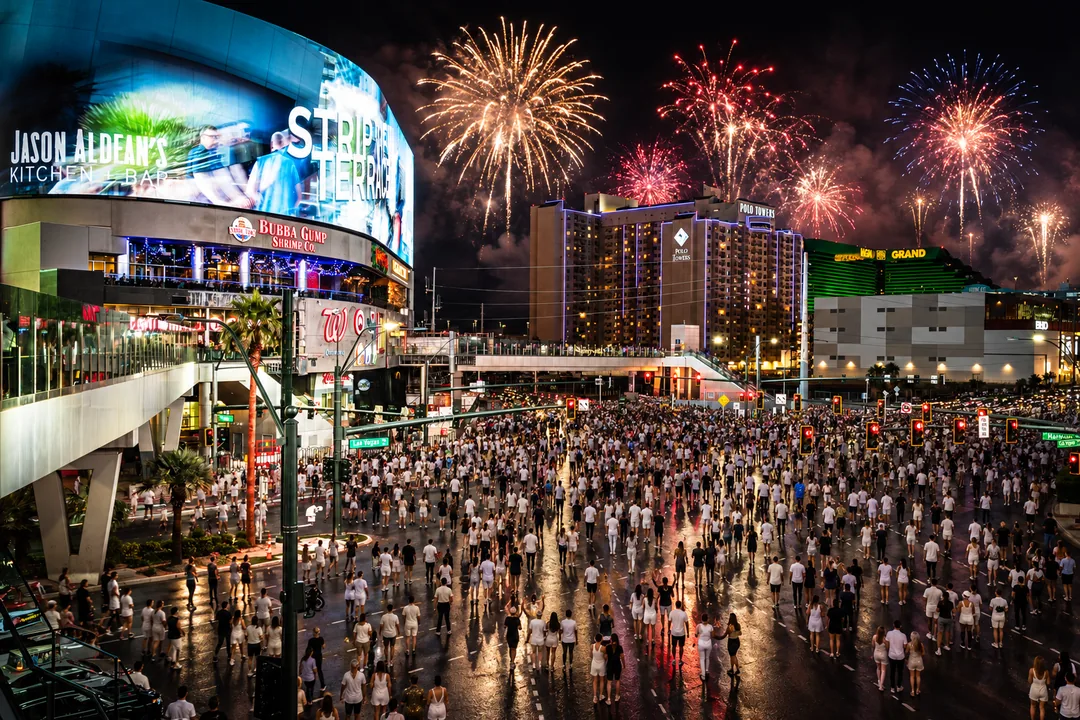 Cena editorial da Las Vegas Strip fechada a carros, com público vestido de branco e fogos no céu noturno