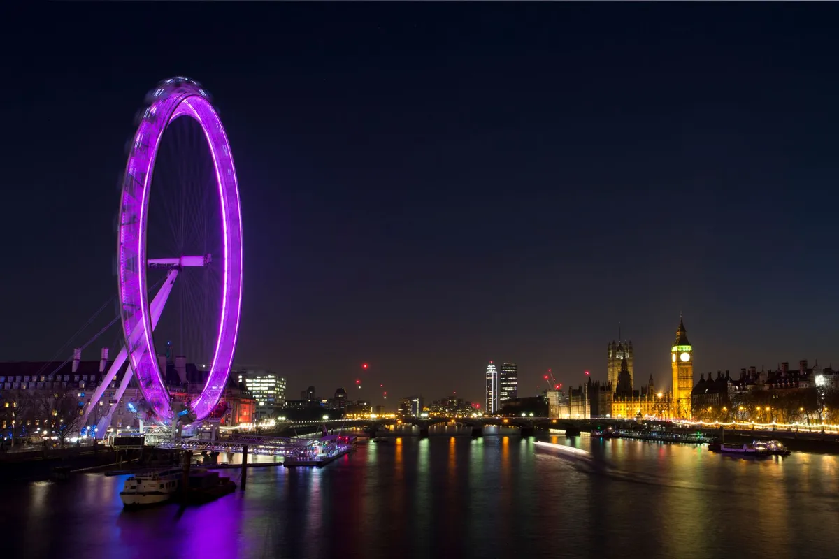 Roda-gigante London Eye iluminada à noite refletida no Rio Tâmisa