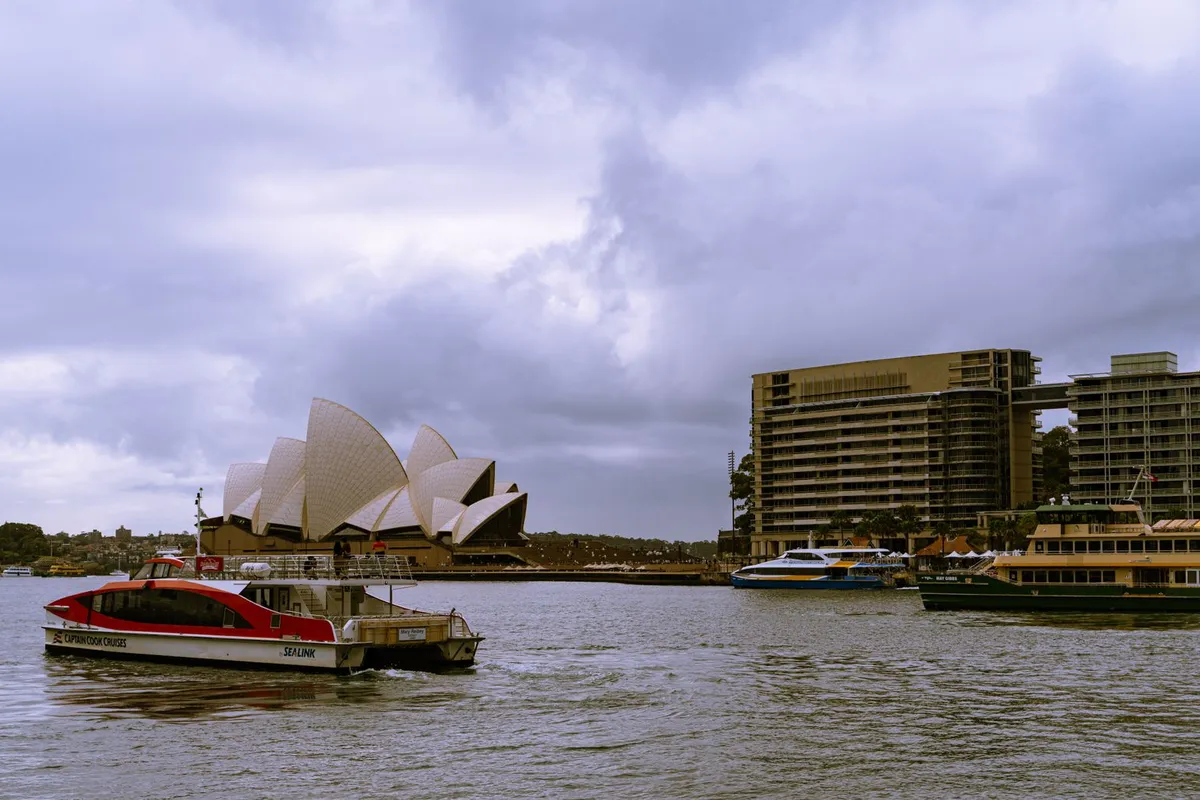 Ópera de Sydney vista da Baía do Porto durante o dia, com a Ponte ao fundo