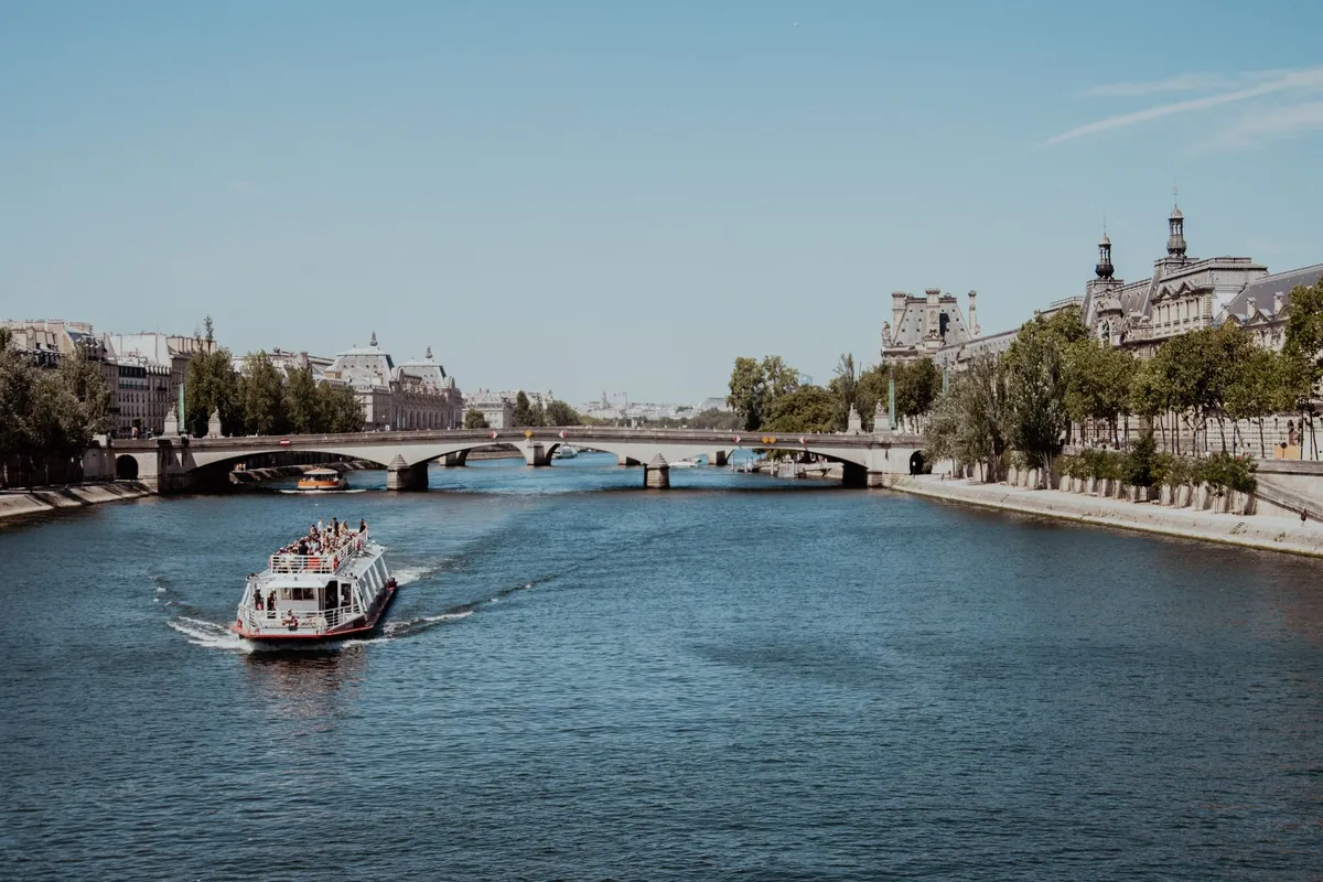 Tourist boat sailing on the Seine River, between bridges and Paris buildings