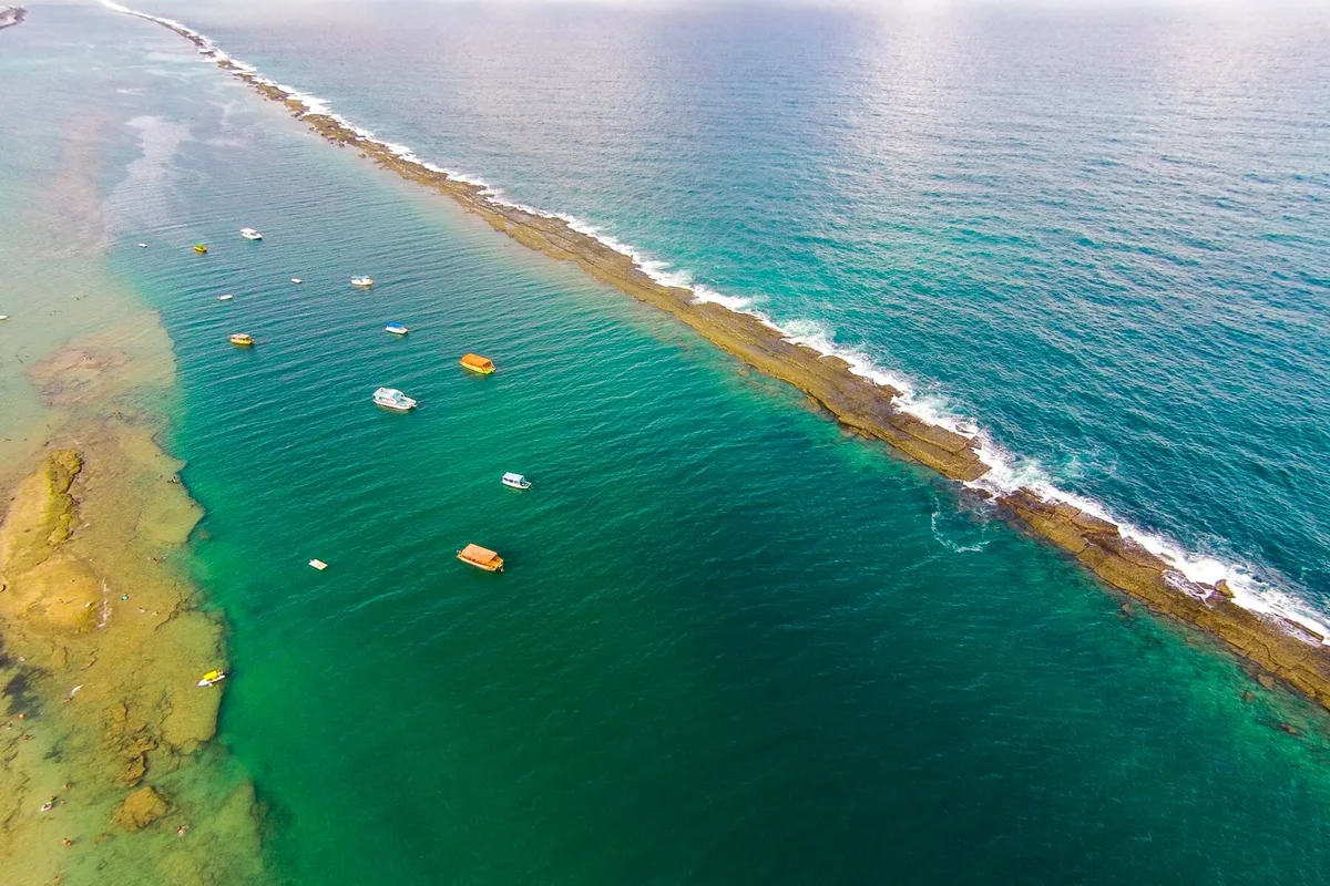 Barrera de arrecifes de la Praia do Francês vista desde lo alto, con barcos en el agua calma del lado izquierdo de la playa
