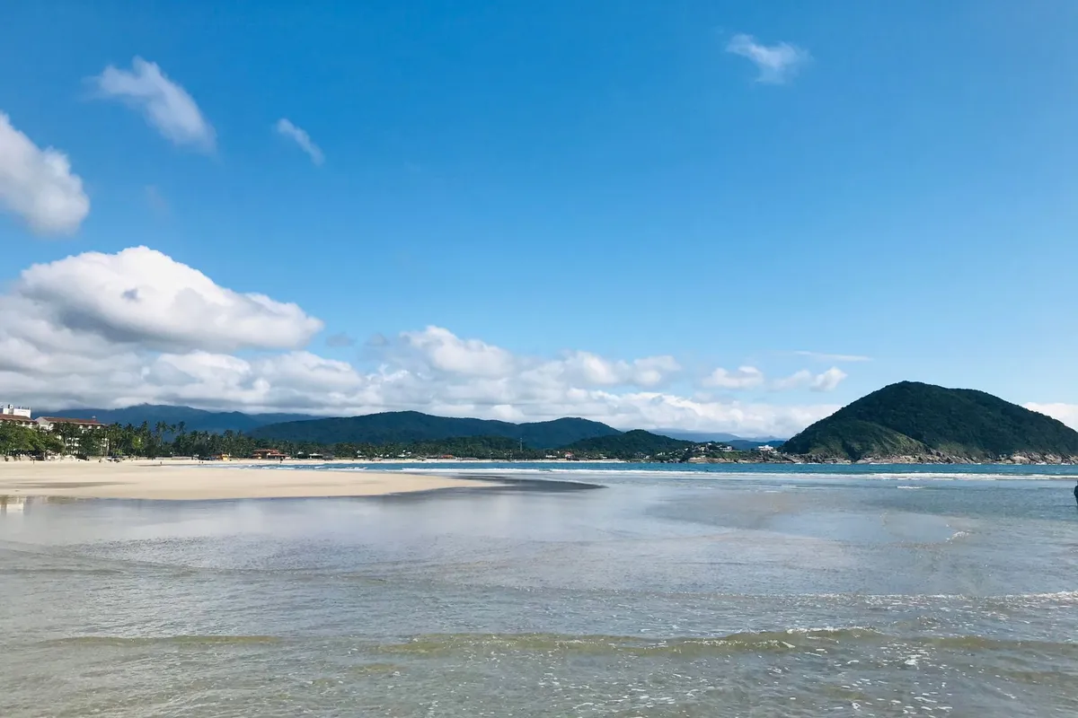 Praia tropical com mar calmo e vegetação no litoral de São Paulo