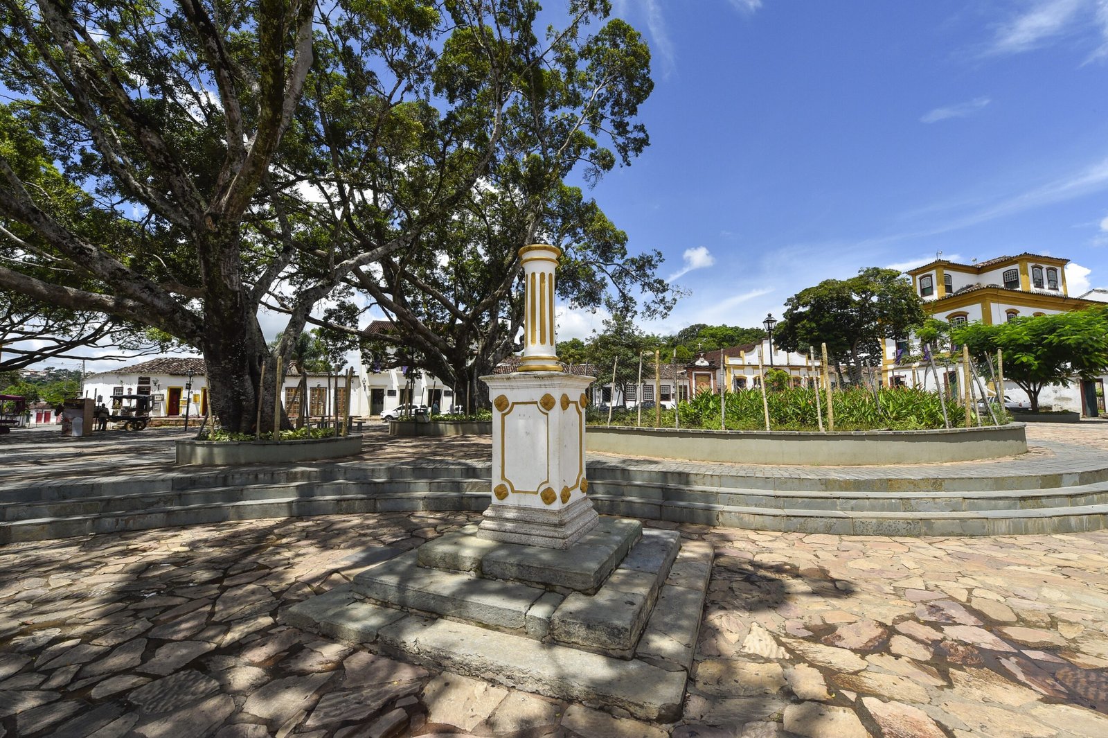 Largo das Forras, em Tiradentes, com árvores, monumento e casas coloniais.