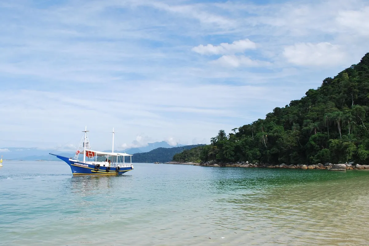 Barco de passeio em águas calmas e verdes de Angra dos Reis, com a mata ao fundo