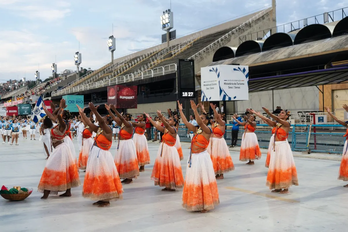 Escola de samba desfila iluminada na Marquês de Sapucaí, vista das arquibancadas e camarotes