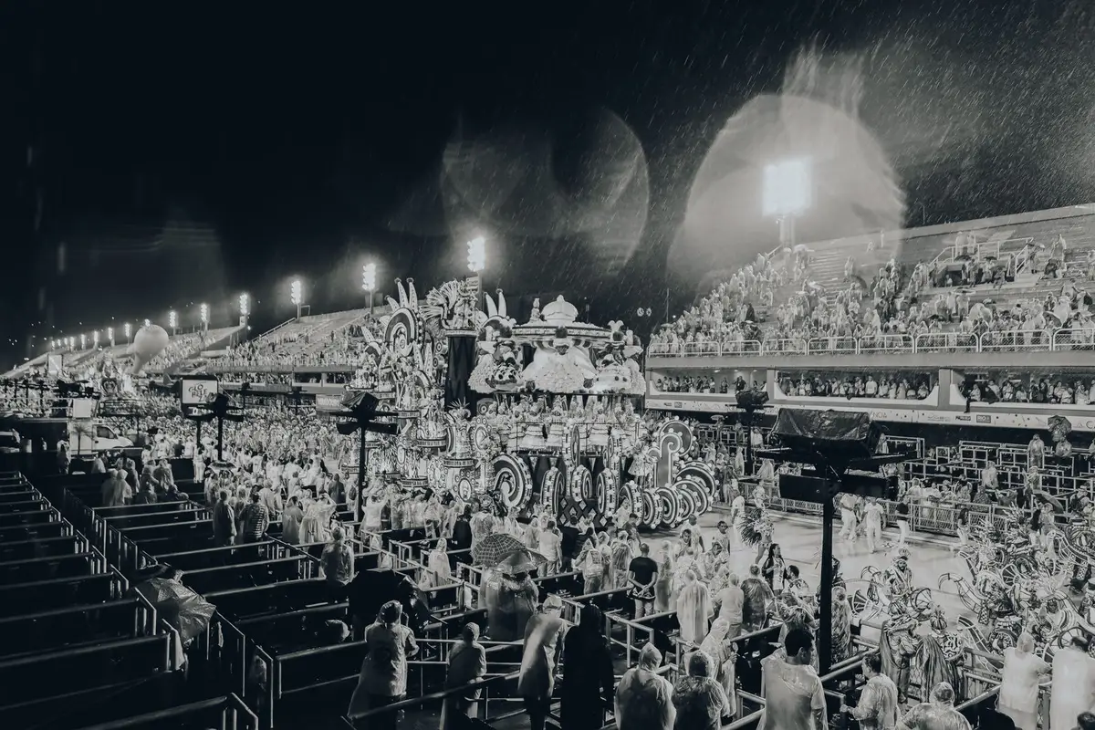 Desfile na Sapucaí sob chuva, com público nas arquibancadas do Sambódromo do Rio