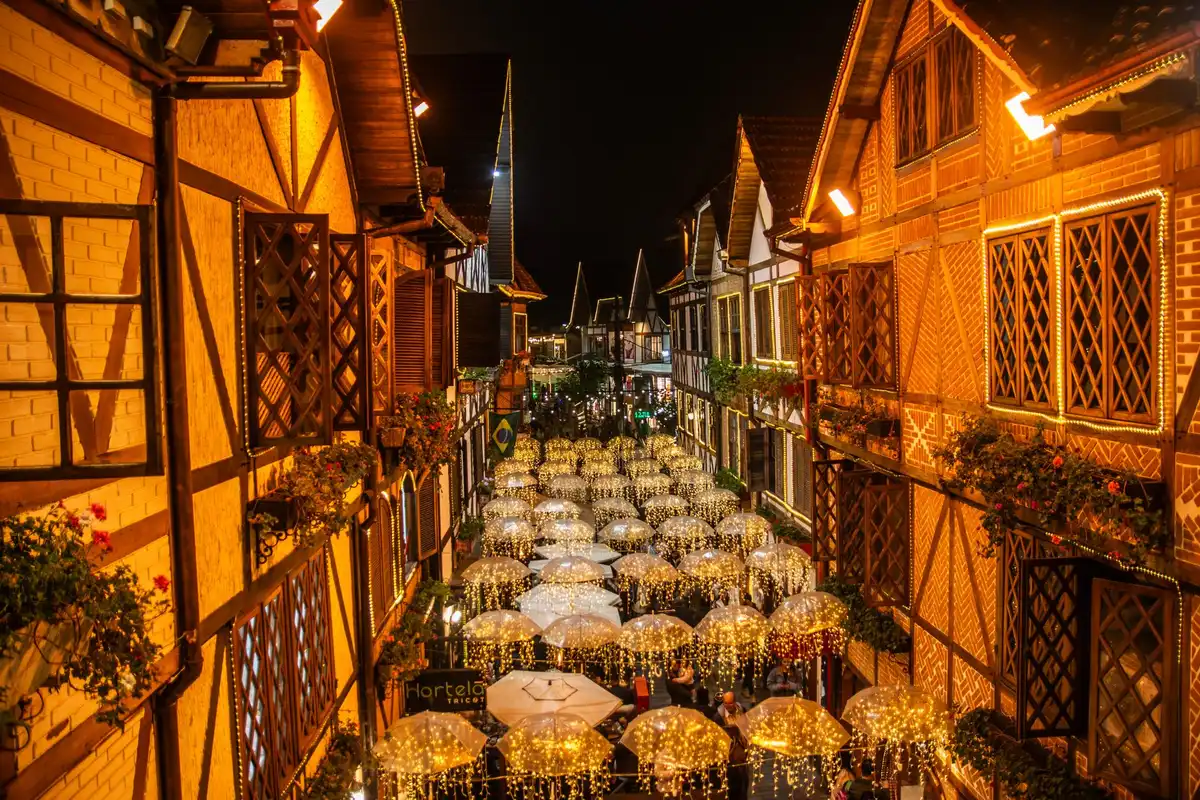 Rua de Campos do Jordão à noite, com guarda-chuvas e luzes de Natal sobre casas de enxaimel