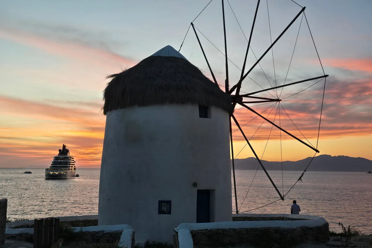 Moinho de vento de Mykonos com navio de cruzeiro ao fundo no pôr do sol