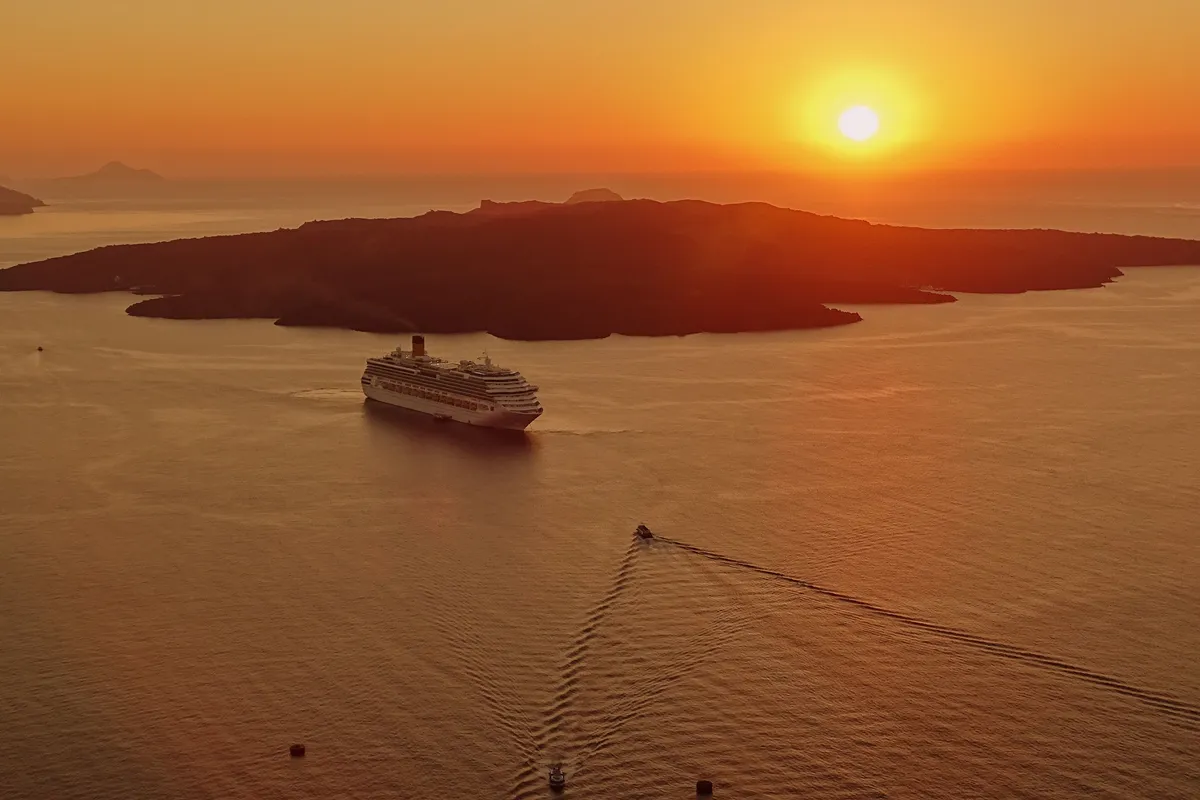 Navio de cruzeiro na caldeira de Santorini ao pôr do sol, com Nea Kameni ao fundo