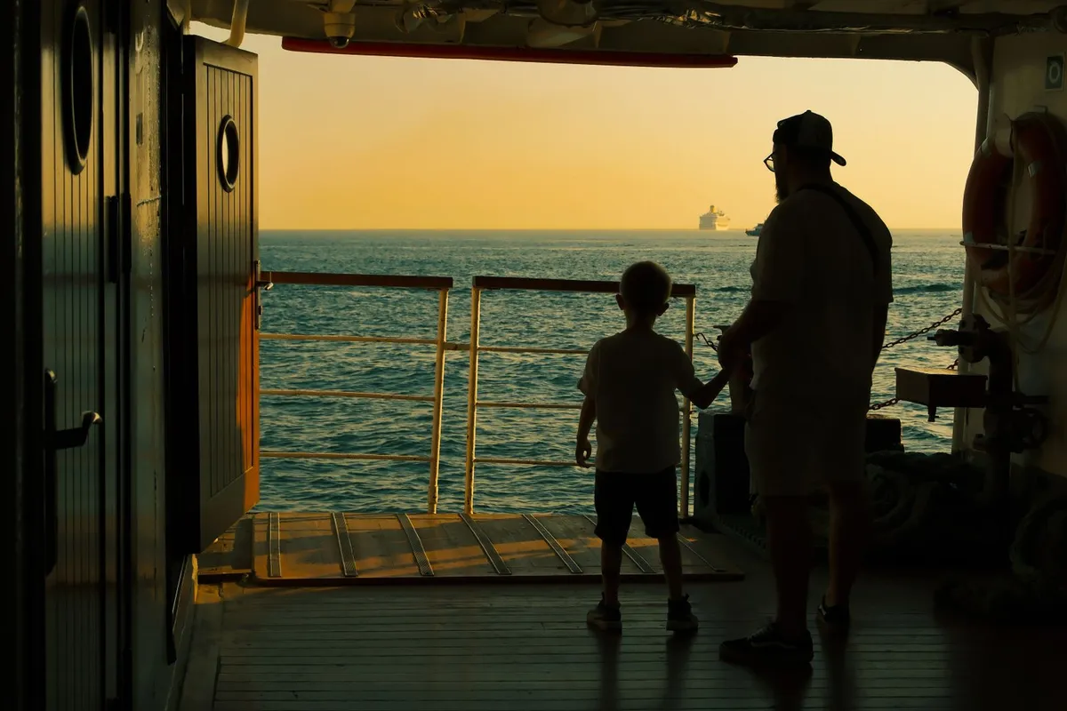 Pai e filho no convés de um navio olhando um cruzeiro no horizonte
