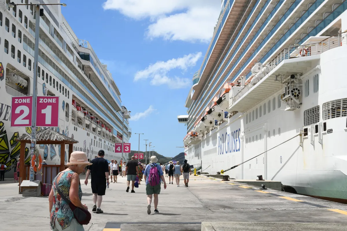 Passageiros caminhando no cais entre dois navios de cruzeiro atracados em dia de escala