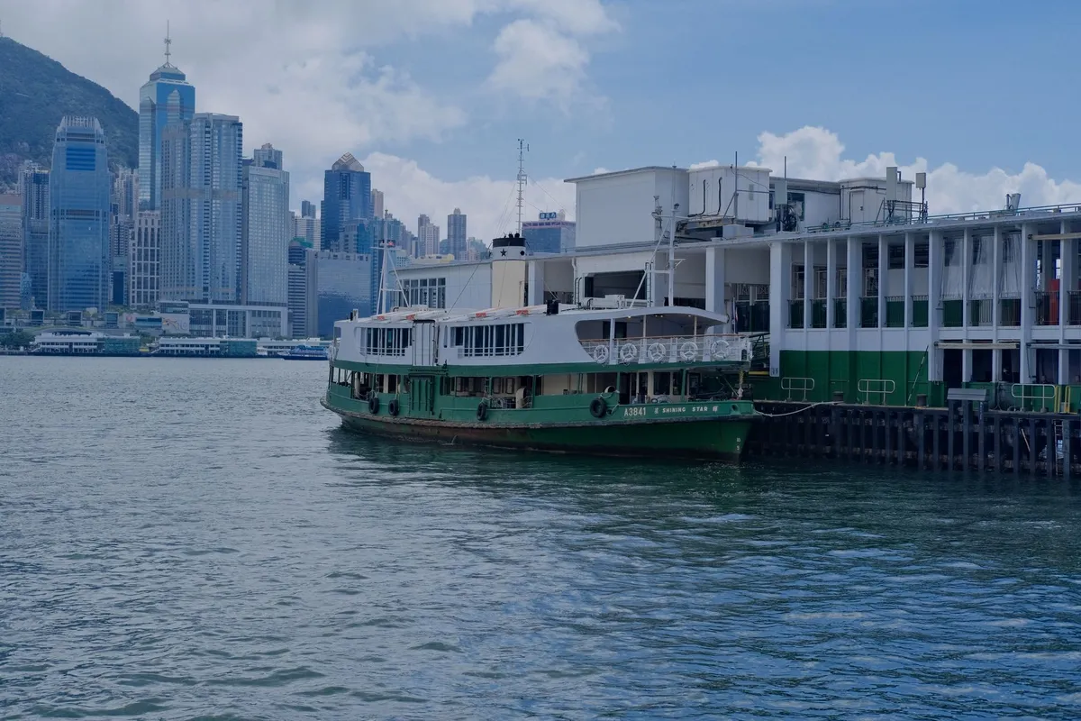 Barco verde e branco da Star Ferry atracado no terminal de Tsim Sha Tsui, com a ilha de Hong Kong ao fundo