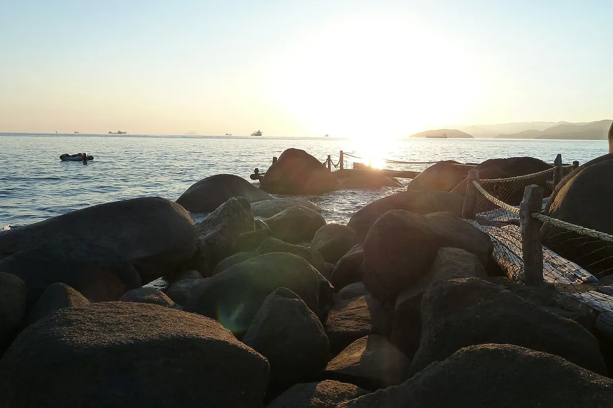 Píer de pedras na orla de Ilhabela ao entardecer, com navios no canal
