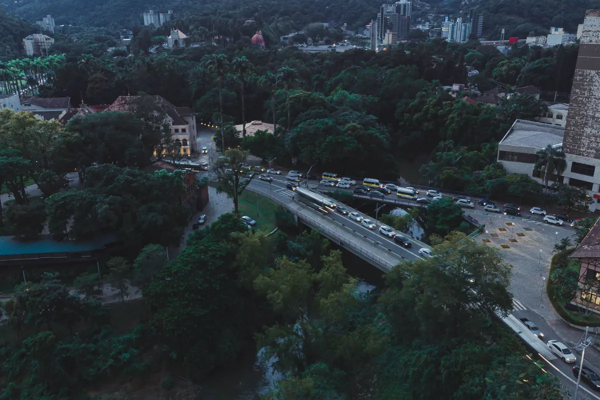 Centro de Blumenau ao anoitecer, com a avenida à beira do rio Itajaí-Açu e luzes acesas