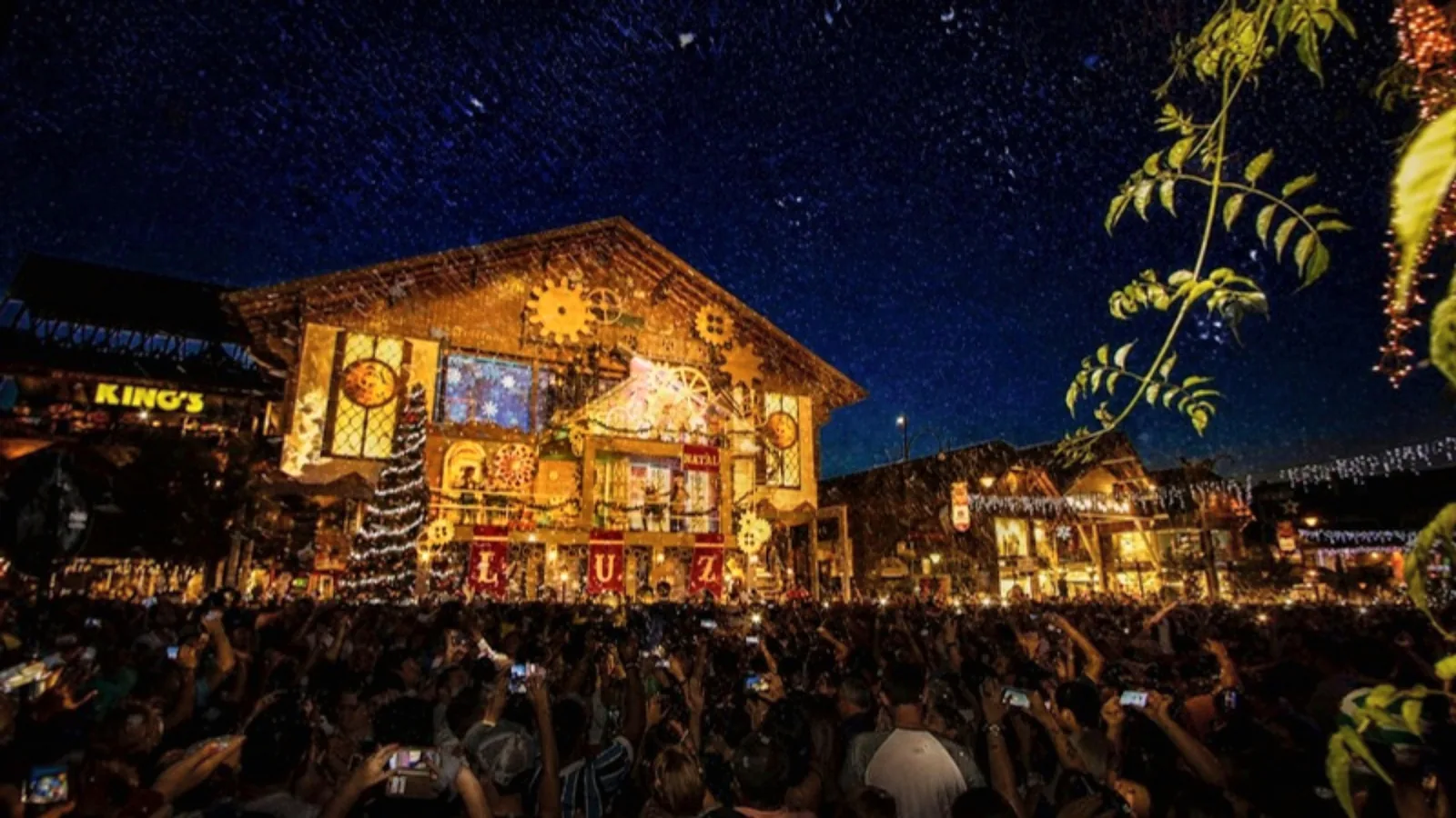 Fachada do Palácio dos Festivais com projeção de luzes de Natal e engrenagens douradas à noite, em Gramado