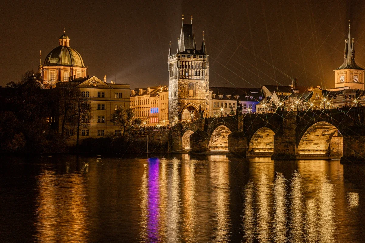 Ponte Carlos e torre da Cidade Velha iluminadas, com reflexos no rio Vltava em Praga