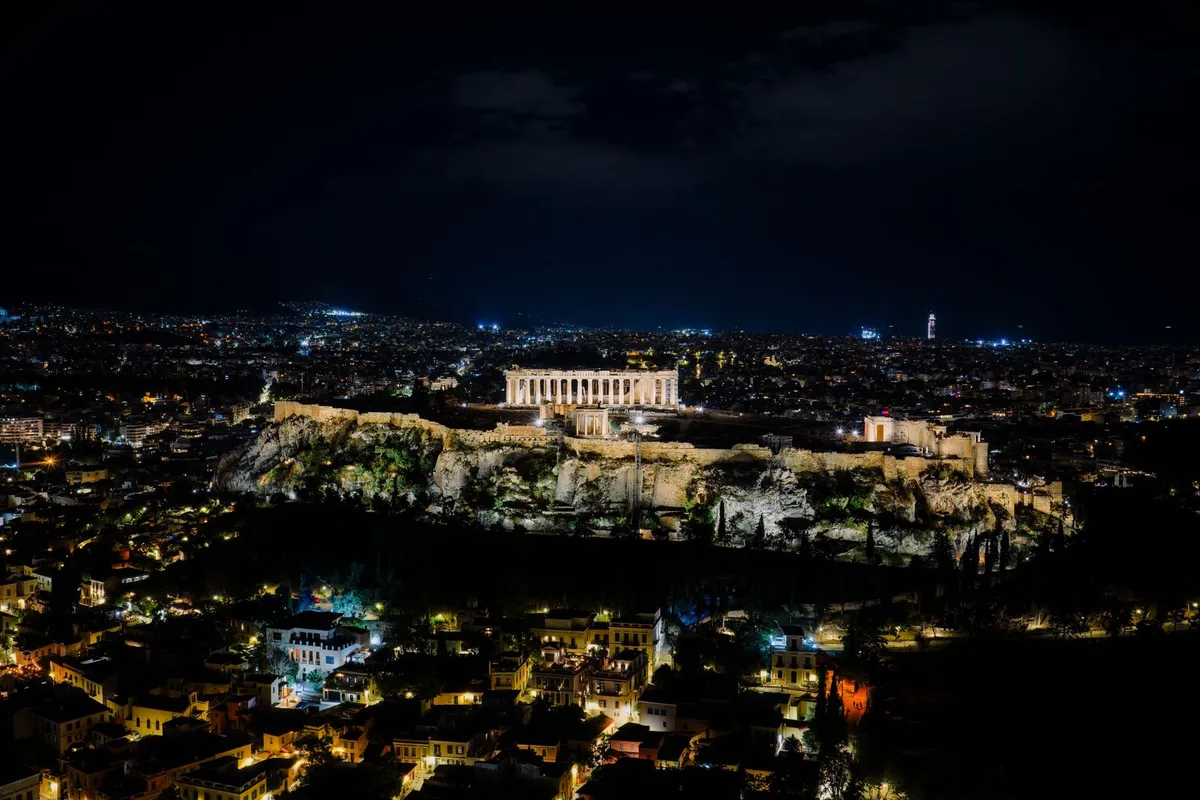 Acrópole de Atenas iluminada à noite, vista do alto com a cidade ao redor, cenário dos fogos do réveillon