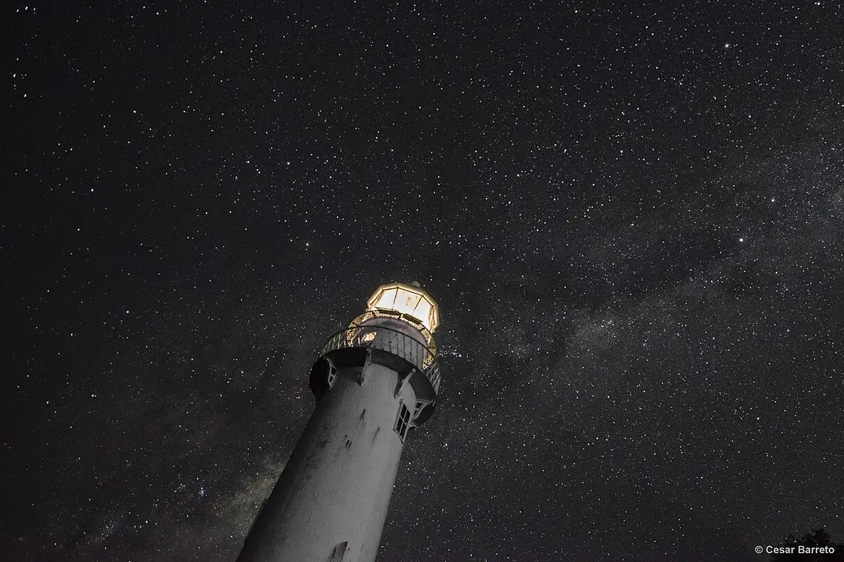 Farol das Conchas iluminado sob céu estrelado na Ilha do Mel, à noite