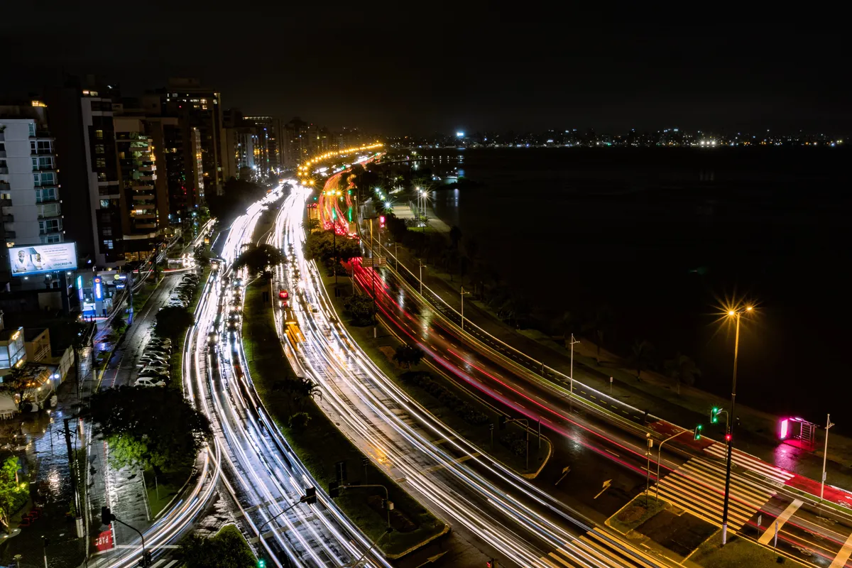 Faróis de carros em longa exposição na orla de Florianópolis à noite, no litoral da ilha onde fica Jurerê Internacional