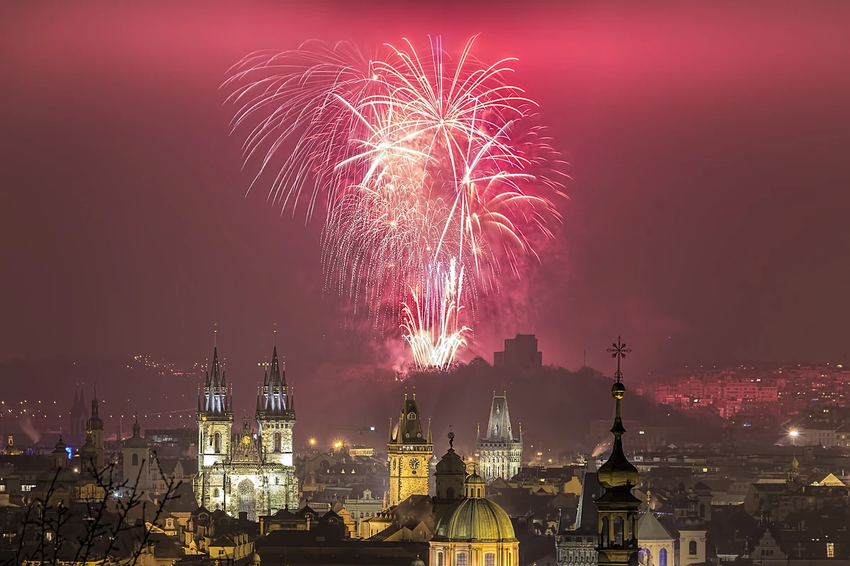 Fogos vermelhos e dourados sobre as torres iluminadas da Cidade Velha de Praga à noite